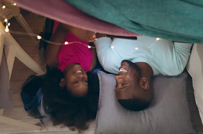 African american girl and her father lying in a fort. staying at home in self isolation during quarantine lockdown.