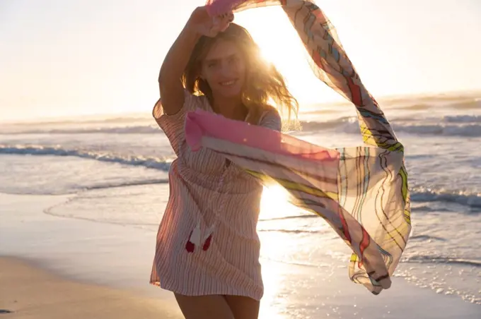 Portrait of caucasian woman holding scarf smiling while standing at the beach. summer beach holiday concept.