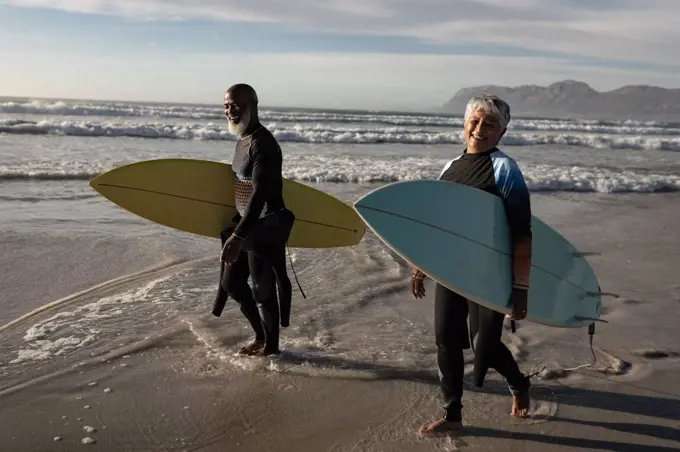 Happy senior african american couple carrying surf boards walking on the beach. travel vacation retirement lifestyle concept