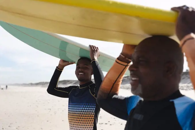 African american father and son carrying surfboards on their heads at the beach. summer beach holiday and leisure concept.