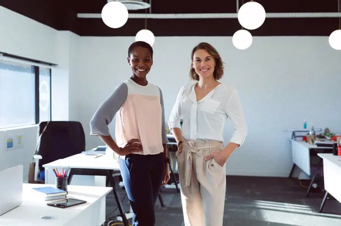 Two smiling diverse businesswomen standing and looking at camera at work. creative business at a modern office.
