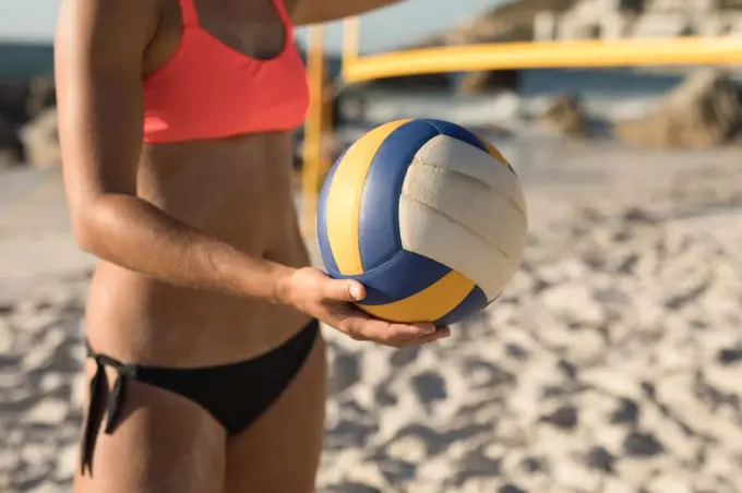 Side view mid section of a Caucasian woman enjoying free time on a beach on a sunny day, holding a ball