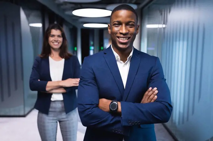 Portrait of diverse businessman and businesswoman with arms crossed smiling at modern office. business and office concept