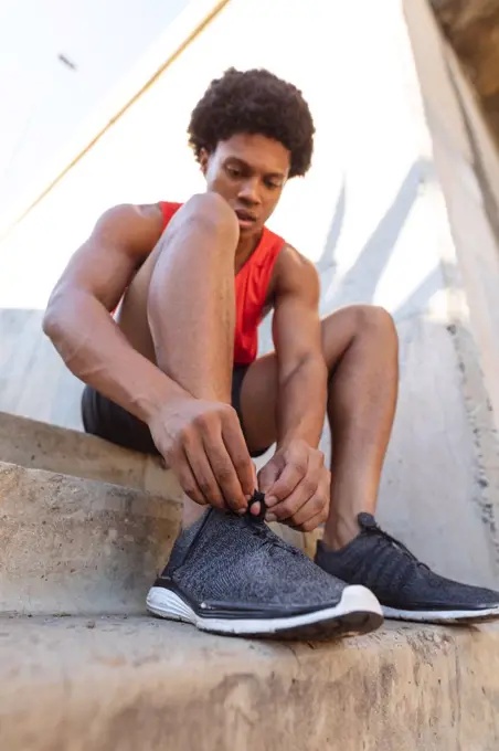 Fit african american man exercising in city tying shoes. fitness and active urban outdoor lifestyle.
