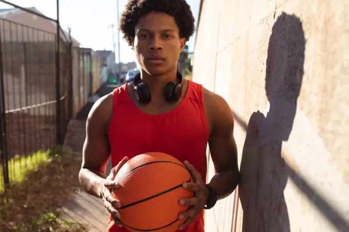 Portrait of fit african american man exercising in city holding basketball in the street. fitness and active urban outdoor lifestyle.