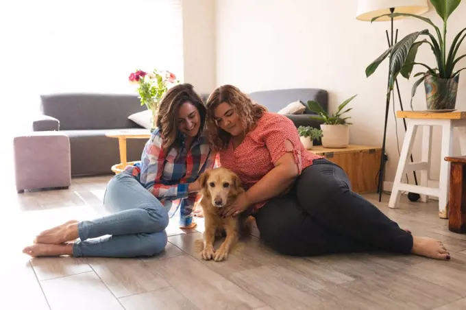 Happy lesbian couple sitting on floor embracing and smiling with their dog. domestic lifestyle, spending free time at home.