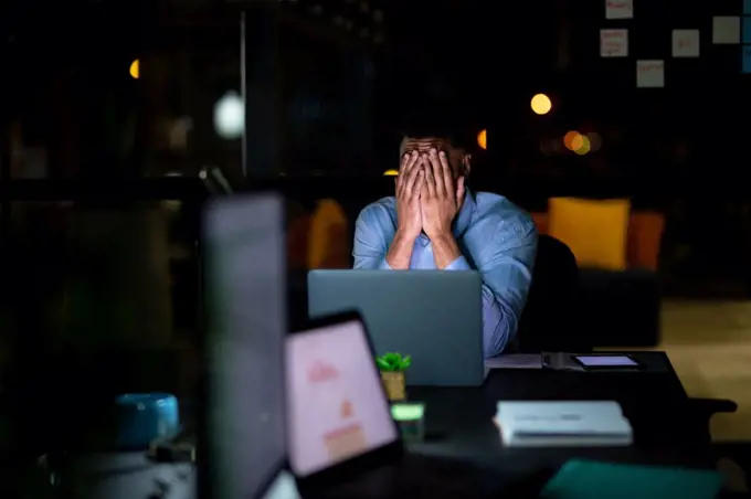 Mixed race businessman working at night, sitting at desk and using laptop. working late in business at a modern office.