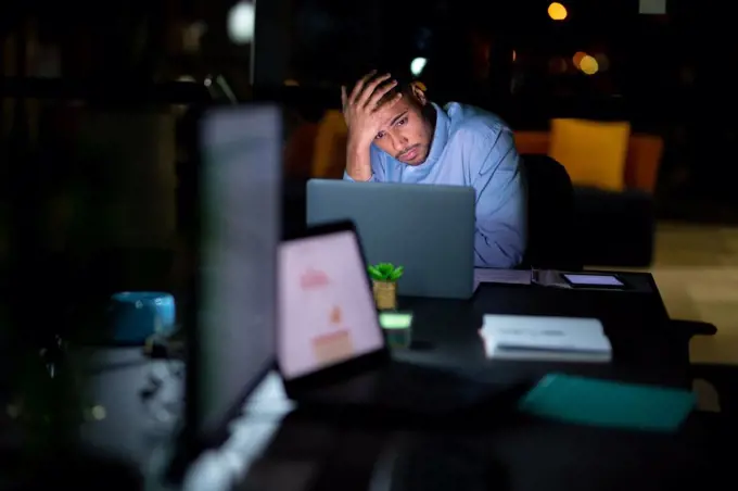 Mixed race businessman working at night, sitting at desk and using laptop. working late in business at a modern office.