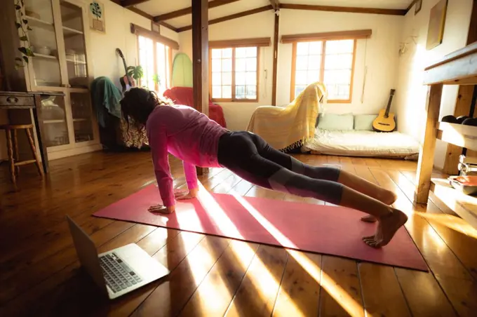 Mixed race woman practicing yoga, doing push ups in sunny living room. healthy lifestyle, enjoying leisure time at home.