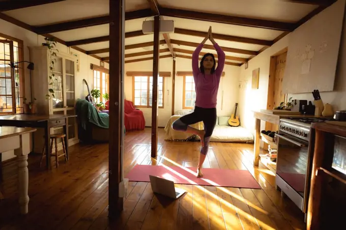 Mixed race woman practicing yoga in sunny living room. healthy lifestyle, enjoying leisure time at home.