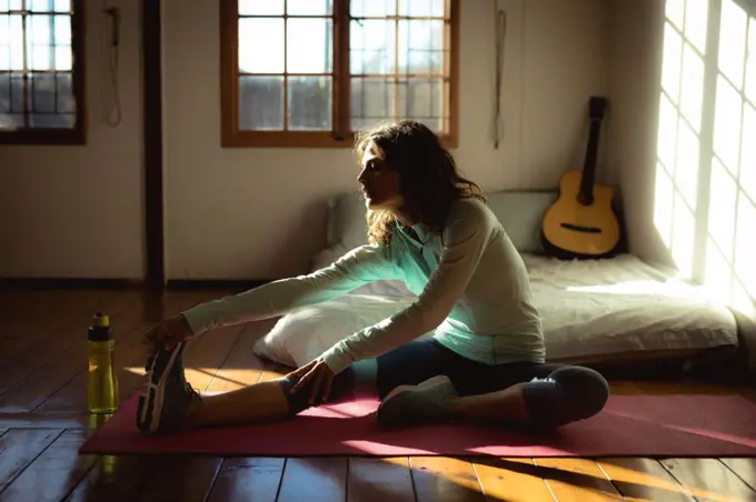 Mixed race woman practicing yoga, stretching in sunny living room. healthy lifestyle, enjoying leisure time at home.