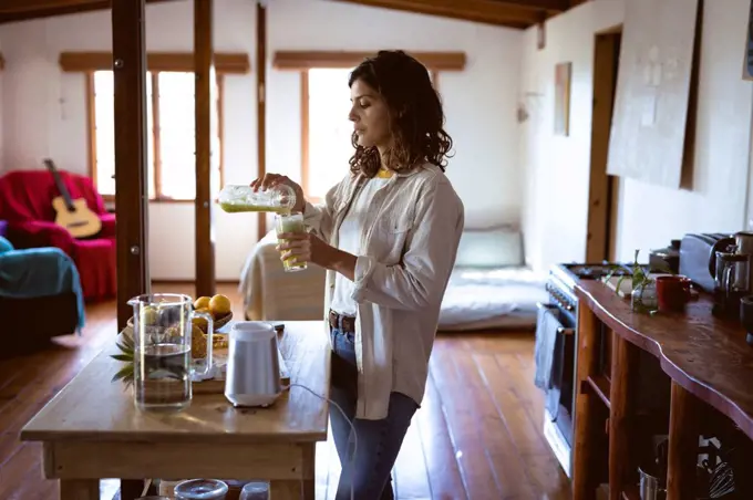 Mixed race woman preparing healthy drink in kitchen. healthy lifestyle, enjoying leisure time at home.