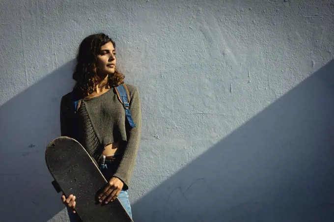 Mixed race woman holding skateboard on sunny day in the street. healthy lifestyle, enjoying leisure time outdoors.