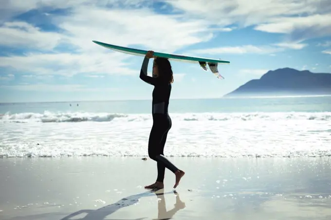 Mixed race woman holding surfboard on sunny day at beach. healthy lifestyle, enjoying leisure time outdoors.