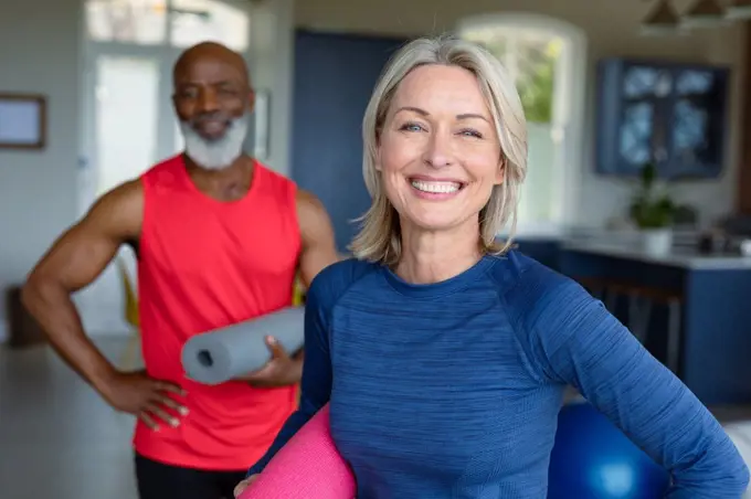 Portrait of happy senior diverse couple in exercise clothes practicing yoga, looking at camera. healthy, active retirement lifestyle at home.