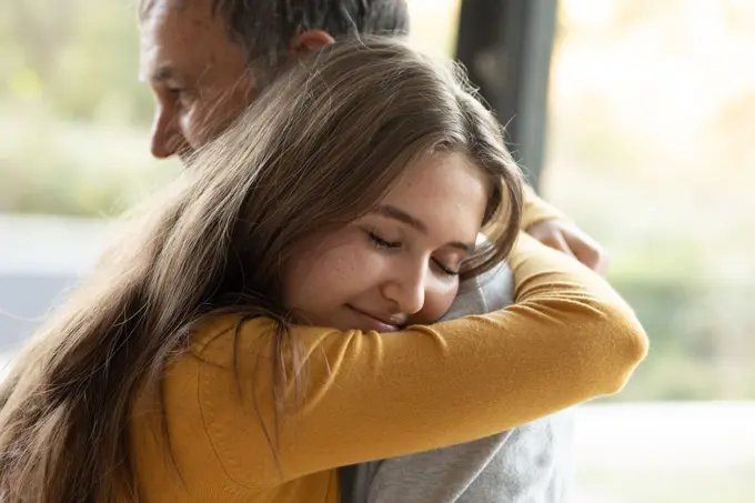 Happy caucasian grandfather and granddaughter hugging at home. family time, active and healthy retirement lifestyle at home.