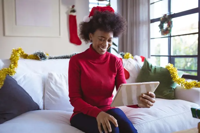 Happy african american woman in santa hat making tablet christmas video call. christmas, festivity and communication technology.