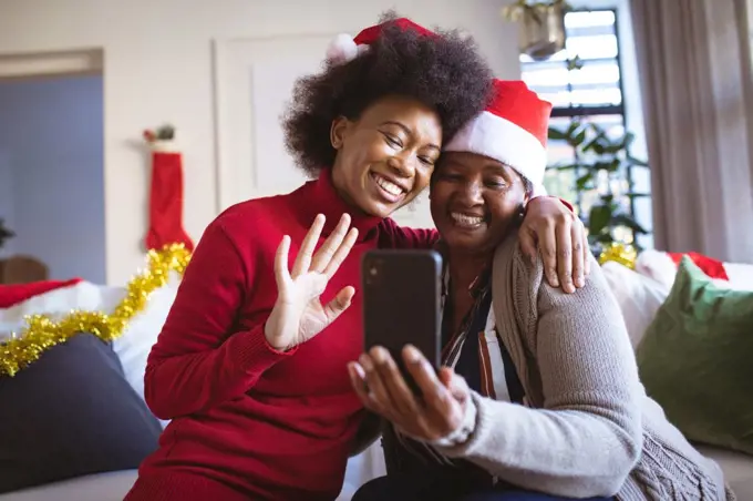 Happy african american senior woman and adult daughter in santa hats making christmas video call. christmas, festivity and communication technology.