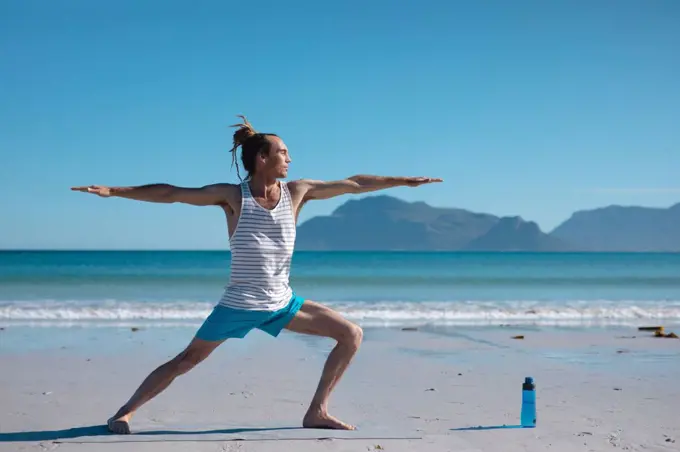 Man practicing warrior 2 pose yoga with arms outstretched at beach against sky with copy space. fitness and healthy lifestyle.