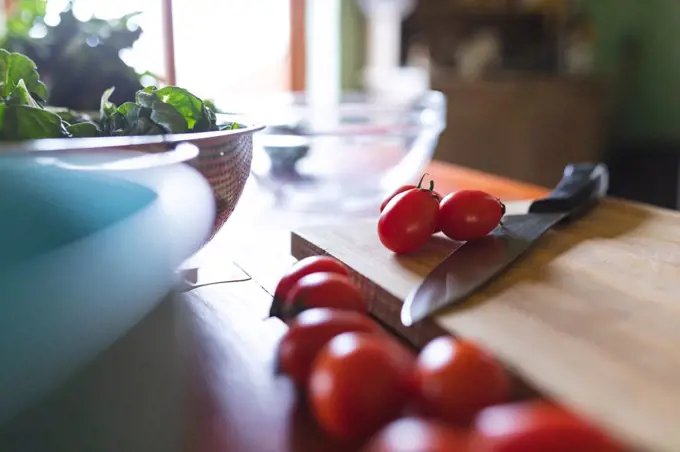 Close-up of fresh red cherry tomatoes with knife on wooden cutting board in kitchen. organic and healthy eating.