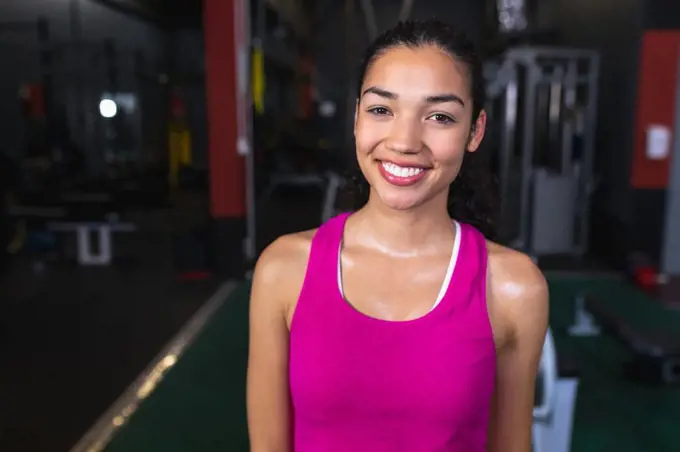 Close-up of Caucasian female athletic looking at camera while standing in fitness center. Bright modern gym with fit healthy people working out and training