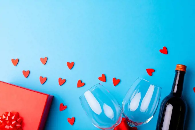 Heart shaped decoration with wineglasses and bottle by gift on blue background, copy space. valentine's day, drink and love concept.