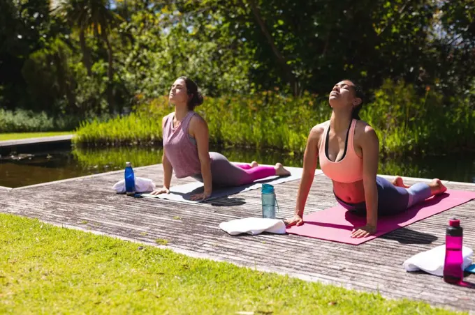 Young women in sportswear practicing yoga on exercise mats at public park. healthy lifestyle and body care.