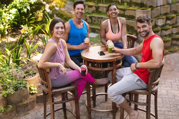 Portrait of happy men and women in sportswear sitting with healthy drinks at table in park. healthy lifestyle, drink and fitness.