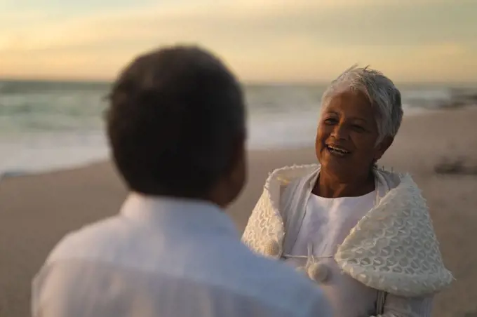 Happy biracial senior woman looking man during wedding ceremony at beach. wedding ceremony, lifestyle and love.