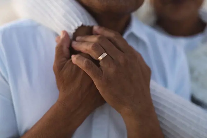 Midsection of senior biracial woman embracing man from behind with wedding ring during sunset. lifestyle, love and weekend.