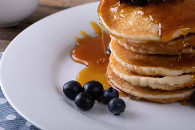 Close-up of stacked pancake served with dripping syrup and fresh blue berries in plate. unaltered, breakfast, sweet food, organic and healthy food concept.