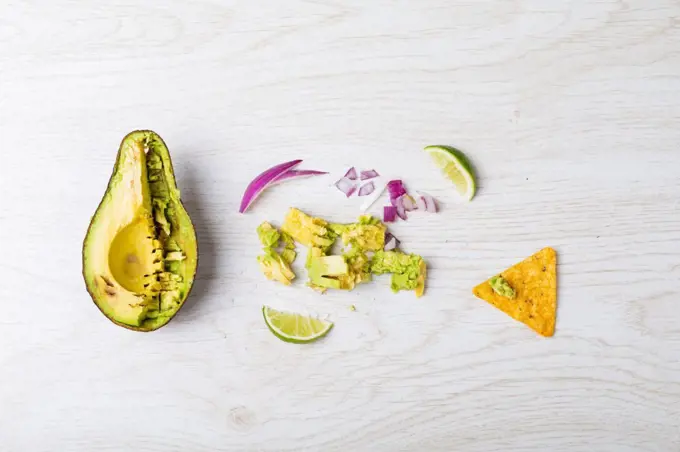 Directly above shot of halved avocado and ingredients on table. unaltered, unhealthy food, snack, preparation, nacho chip, crunchy and savory food.