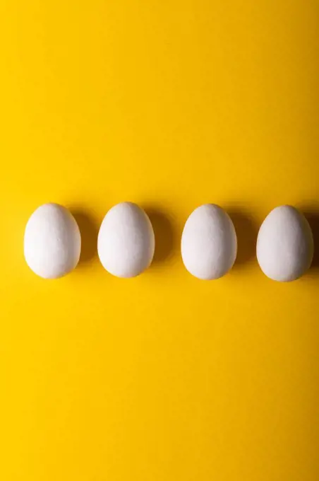 Directly above view of fresh white eggs arranged side by side against yellow background. unaltered, food, healthy eating concept.