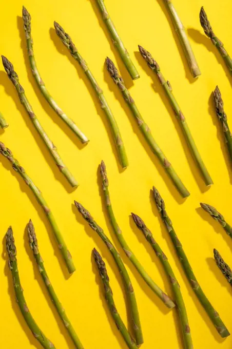 Overhead view of scattered raw green asparagus over yellow background. unaltered, food, healthy eating and organic concept.