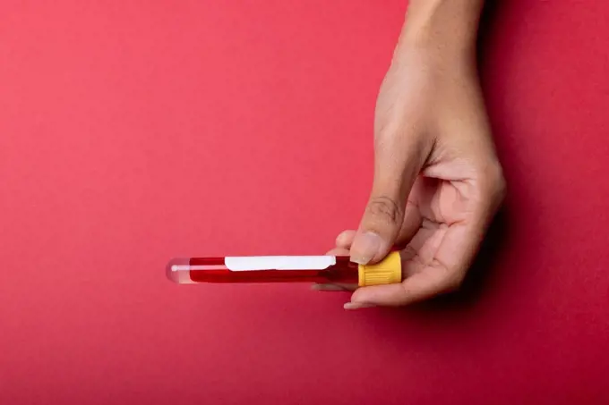 Cropped hand of african american mid adult woman holding test tube with blood on red background. copy space, blood, test tube, medical, sample, laboratory and healthcare concept.