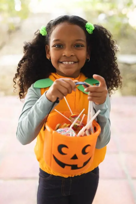 Vertical image of happy african american girl in halloween costume with basket. Halloween, american culture and celebration concept.