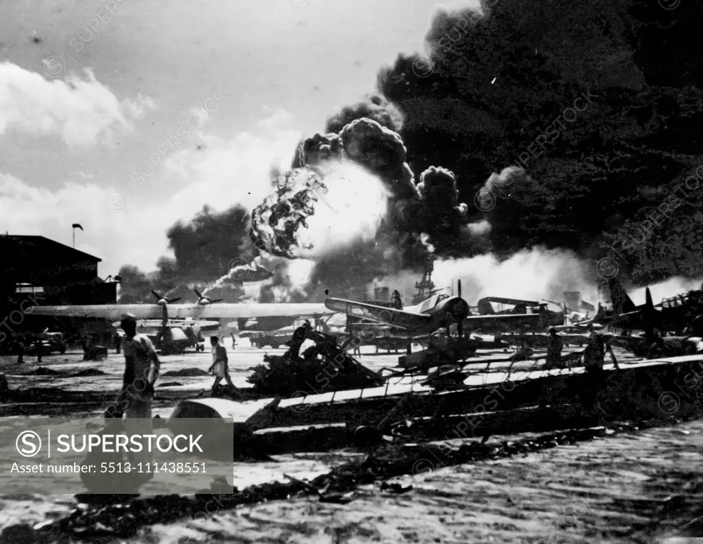 Against a background of smoke and flame, wreckage-strewn Naval Air Station is shown after one of the sneak attacks by Jap bomber on Pearl Harbor, on December 7th, 1941. Note wing of blasted patrol bomber, (foreground) huge ball of flame (background) came from explosion that happened just as this photo was taken. Picture was just released by the Navy Department in Washington. February 4, 1943.