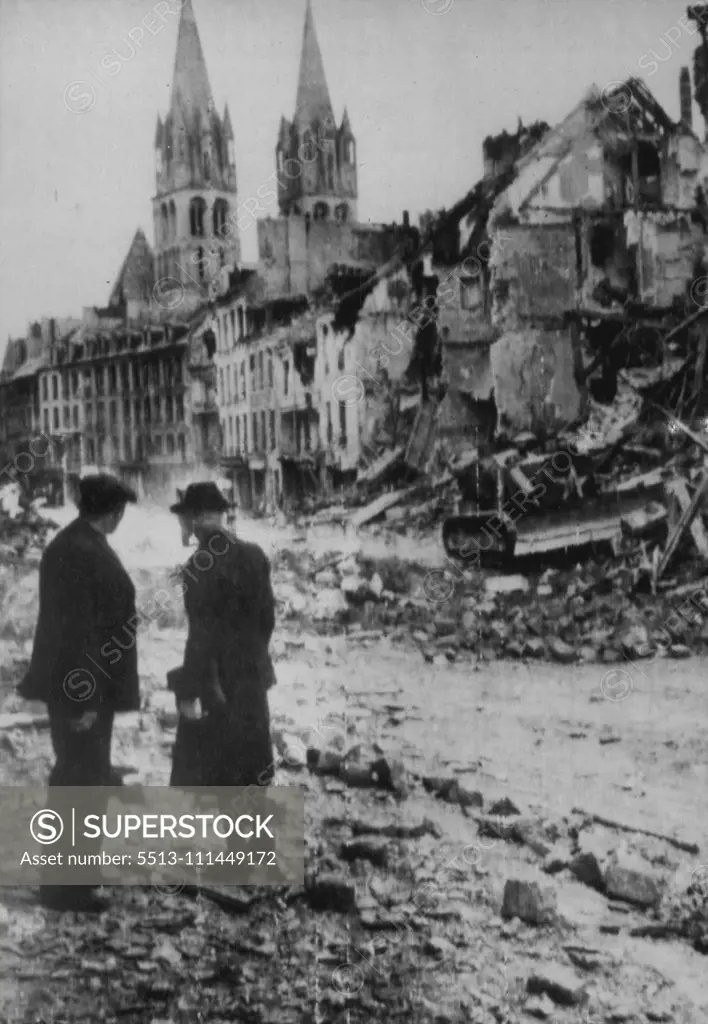 Church Spires Survive Bombardment -- Two French civilians gaze at the twin spires of a church in Caen, France, which stand almost unscathed amid the wreckage of surrounding buildings badly damaged by heavy barrage which preceded the downfall of the former German strongpoint in Normandy. December 07, 1944. (Photo by Associated Press Radiophoto).