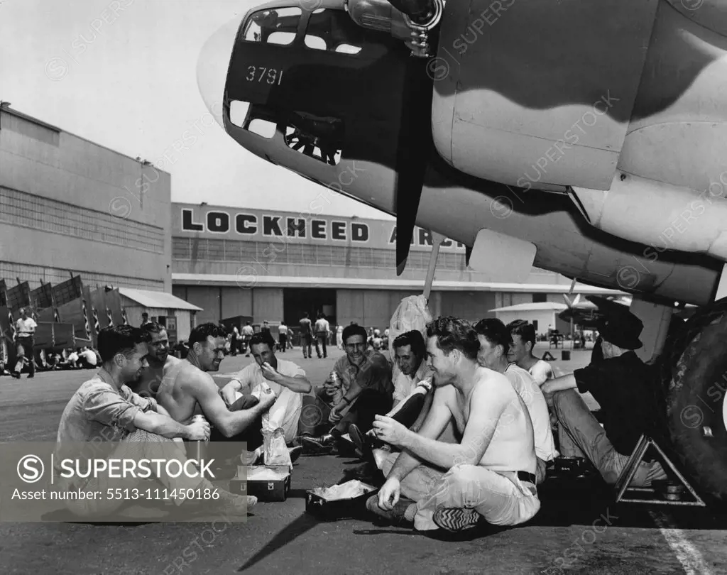 A bunch of the boys eat an Al Fresco lunch under the nose of a Lockheed Bomber they helped to build. They're kidding Palmer, (third from left) about his build. "Hey Superman!" one of them chortles between bites," when are you Gonna fly one o' these bombers to England.... on your back, I mean". July 18, 1941. (Photo by ACME).