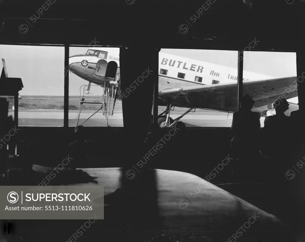 Passengers view a DC3 of ***** BAT fleet through the windows of the terminal at Mascot. November 30, 1955.