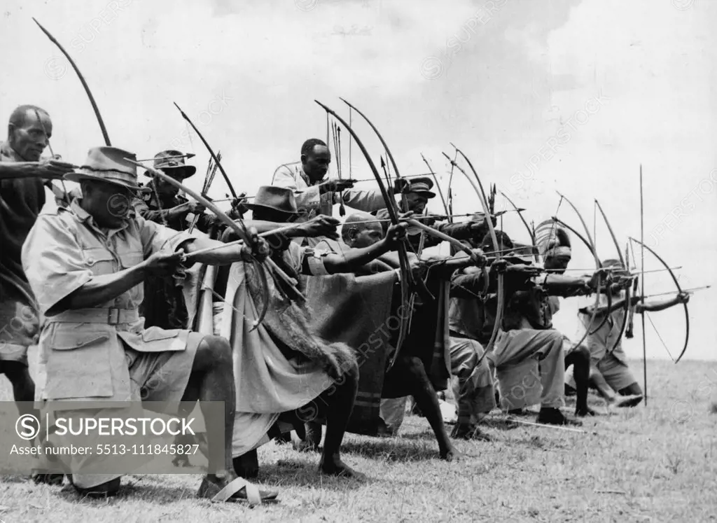 Bows And Arrows Are Weapons Of Loyal Kikuyu -- Men of the Kikuyu home guard show their prowess with bows and arrows during the first big exercise of the Home Guard near Githunguri. Although the dreaded Mau Mau gangs are drawn mostly from the kikuyu tribe, other members have formed the Home Guard to prevent the growth of Mau Mau in the area. Arms have been given to them after careful 'screening'. Some walked as far as 20 miles to take part in the exercise, bringing with them an assortment of weap