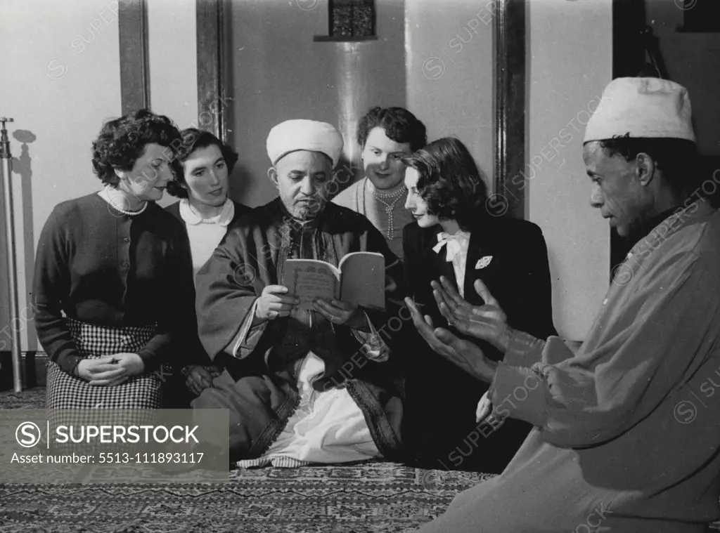 In a mosque in Cardiff's dockland, four British converts to the Moslem faith listen as the Imam of the mosque, Abdulla-El-Hakin, reads to them from the Koran - the Moslem Bible. Kneeling on the right is Ali Mohammad, one of the Mosque dignitaries. Scenes like this are not unusual in Cardiff. The Arabs in Tiger Bay - the dockland area - number 3,000, forming the largest Moslem community in Britain. Many of them marry Christian girls, and in most cases when that happens the girls adopt the faith o