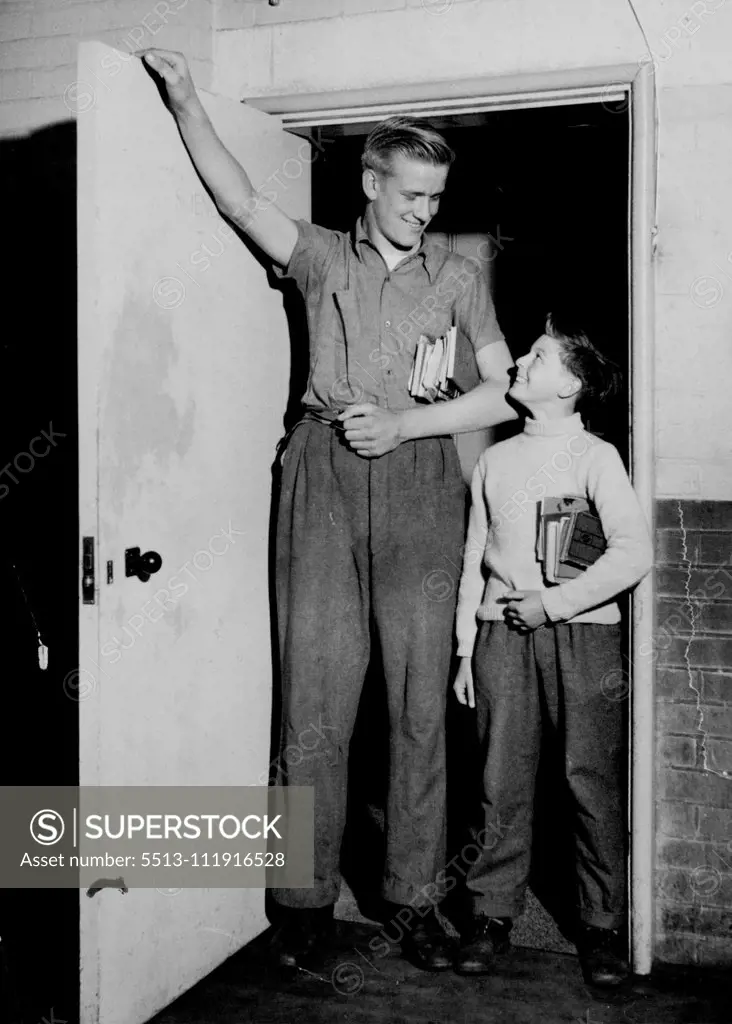 Fourteen year old John Parker (6ft. 7in. tall) "heads" the door of his home in Florence-road, Parkstone, Dorset. With him is his brother, Michael, normal sized, but looking tiny. And John has two sisters, also normal-sized. September 19, 1955. (Photo by Daily Mirror).