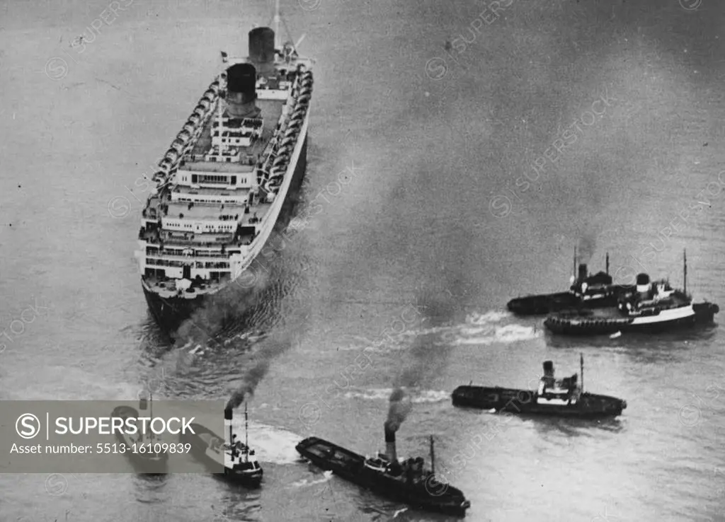 "Queen Elizabeth" Runs Aground -- An aerial photograph shows the giant liner firmly aground as six tugs attempt to drag her clear. The Cunard liner "Queen Elizabeth", the world's largest liner, with 2,446 passengers and a crew of 1,200 aboard, has run aground at the entrance to Southampton water during a dense fog. The 85,000 ton ship was returning to Southampton from New York. Twelve tugs have so far failed to move her. April 23, 1947. (Photo by Sport & General Press Agency Limited).