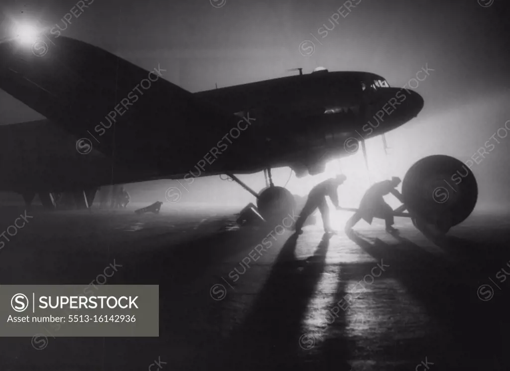 Backing Up The "Air-Lift" -- Honington is busiest at night, when aircraft are loaded so that at first light they may take off for bases in Germany. Here a giant wheel for a York aircraft, grounded at Wunstorf, Germany, is trundled out to a waiting Dakota of "Operation Plumber." An important if unspectacular link in the maintenance of the Royal Air Force's contribution to the "Air-Lift" into blockaded Berlin is "Operation Plumber." This is the R.A.F.'s name for the major servicing unit of transport Command at Honington, Suffolk, where a fleet of six Dakota are kept busy flying unserviceable aircraft parts back from Germany and taking out immediate replacements. November 24, 1948. (Photo by Associated Press Photo).