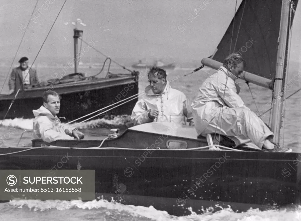 All-round sportsman the Duke of Edinburgh at the helm of the yacht Bluebottle, competing in a race at Cowes Regatta. The Duke is a good cricketer and polo player. On a downwind run at a Cowes regatta, Duke of Edinburgh steers Dragon class Bluebottle which has good chance of winning right to represent at the Melbourne Olympics. Uffa Fox is the burly fellow standing in the cockpit. August 25, 1953.