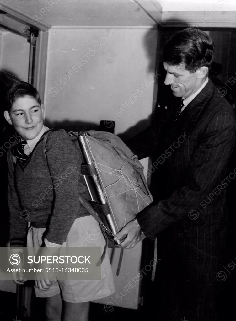 Anthony Malcolm, 12, son of New Zealand senior Trade Commissioner in Sydney, J. Malcolm, carries Mt. Everest conqueror Sir Edmund Hillary's pack to the customs room at Rose Bay flying boat base this morning, when Sir Edmund left by Teal for Auckland. Mr. Malcolm and Anthony saw Sir Edmund off. August 8, 1953.