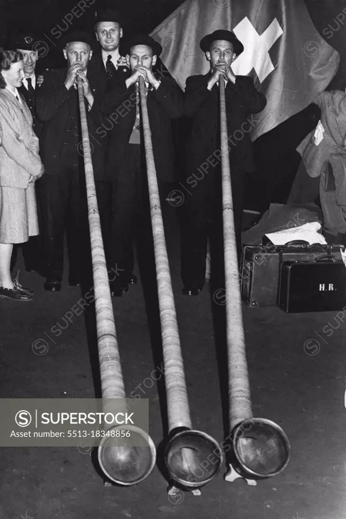 The Alphorns Are Here -- Members of the Swiss team blowing a short motif on the giant horns.158 members of the Union Folk - Iorique Suisse arrived today - they are men and women yodelers from around lake Lucerne; they will assist at a concert of folk music an dancing in Buckingham palace Gardens on Queen Mary's birthday. With them they brought the 12ft. long alphorns, which they will blow. May 24, 1948.