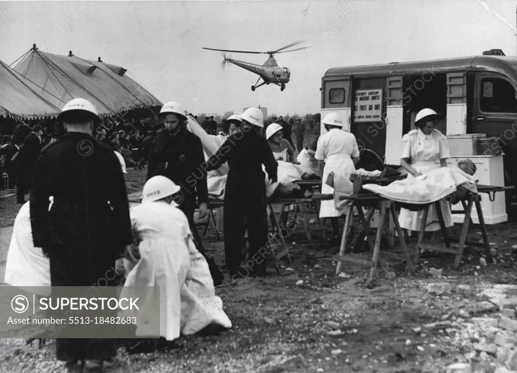 Helicopter Used In Civil: Defense Training Operation -- Nurses and Civil Defense workers dealing with "casualties" at the demonstration this afternoon, while the helicopter which was used to assist in the demonstrations, flies overhead. The Rt. Hone Sir David Maxwell Fyfe, Q.C. M.P. Secretary of State for the Home Department, today opened the Bully Fen Rescue Training Ground at Hackney, East London, after which demonstration was given by members the Civil Defence Services. April 15, 1953. (Photo by Fox Photos).