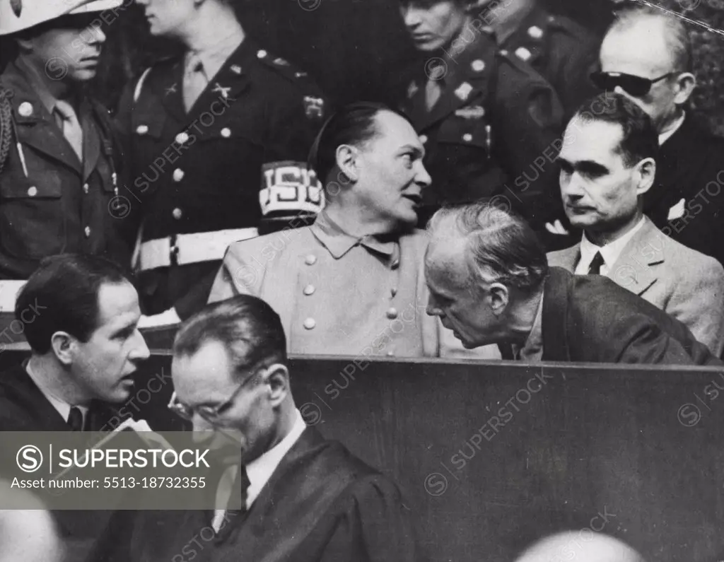 Nazi war criminals whisper in the dock at Nuremberg. Joachim von Ribbentrop leans in front of Rudolf Hess to confer with his lawyer (lower left), whille Hermann Goring (centre), turns to speak to Karl Dontiz (rear right). The trial still drags on. April 18, 1946. (Photo by Associated Press Photo).